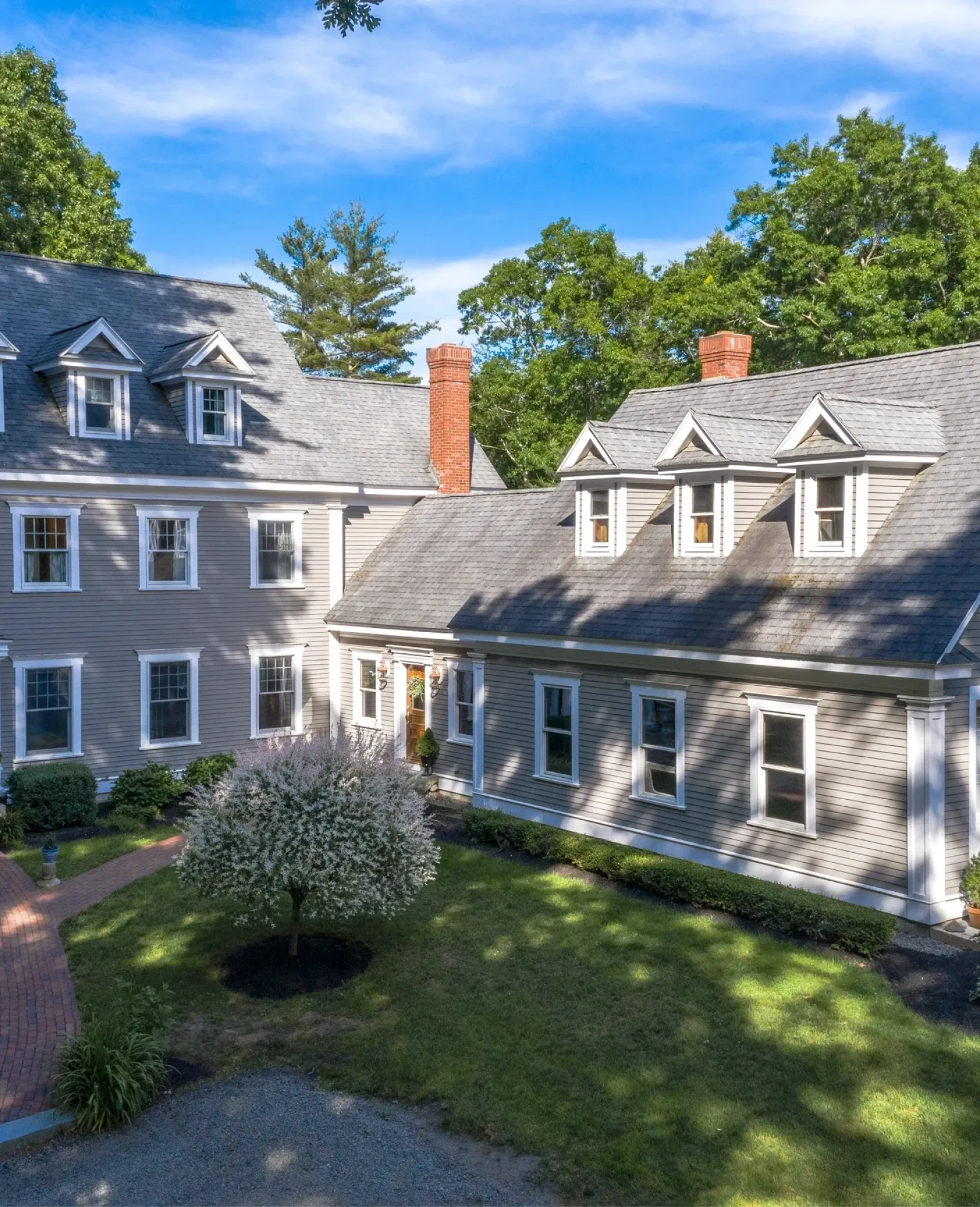 Colonial-style house with gray exterior and trees.